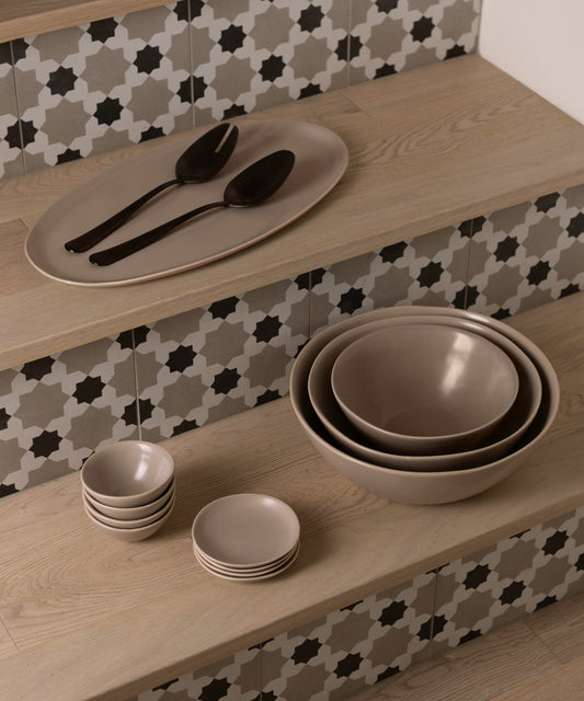 Fable desert taupe stoneware platter with black serving spoons, nested bowls and small dishes on wooden steps with patterned tile