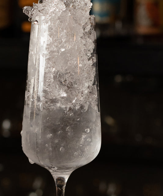 Close-up of a Fable champagne flute filled with crushed ice and sparkling water against a dark bar background