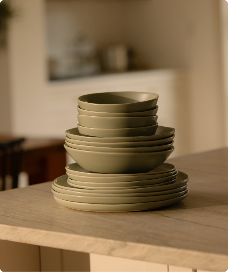 Stack of Fable olive green matte stoneware plates and bowls on a wooden kitchen island