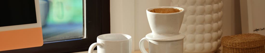 White ceramic pour-over coffee dripper resting on a mug on a windowsill counter