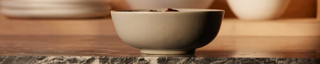 Grey ceramic bowl with food on a marble surface, additional bowls blurred in background