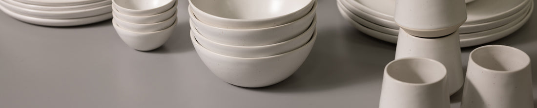 Stacked white ceramic bowls, plates, and cups arranged on a grey surface