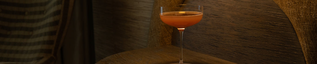 Amber cocktail in a coupe glass on a warm-lit wooden surface