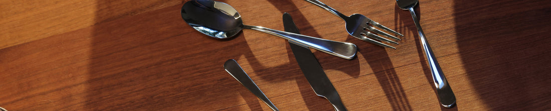 Silver stainless steel flatware including spoon, fork, and knives arranged on a warm wood surface