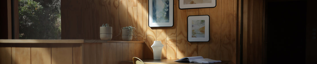 Warm-lit wood-paneled room with framed art prints, a white vase, and potted succulents
