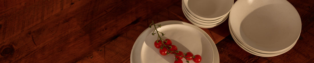 Stacked cream dinner plates and bowls on a rustic wooden table with cherry tomatoes