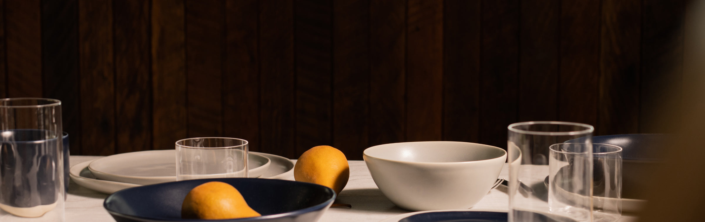 Fable white and navy dinnerware with clear glasses and lemons on a marble table against a dark wood wall