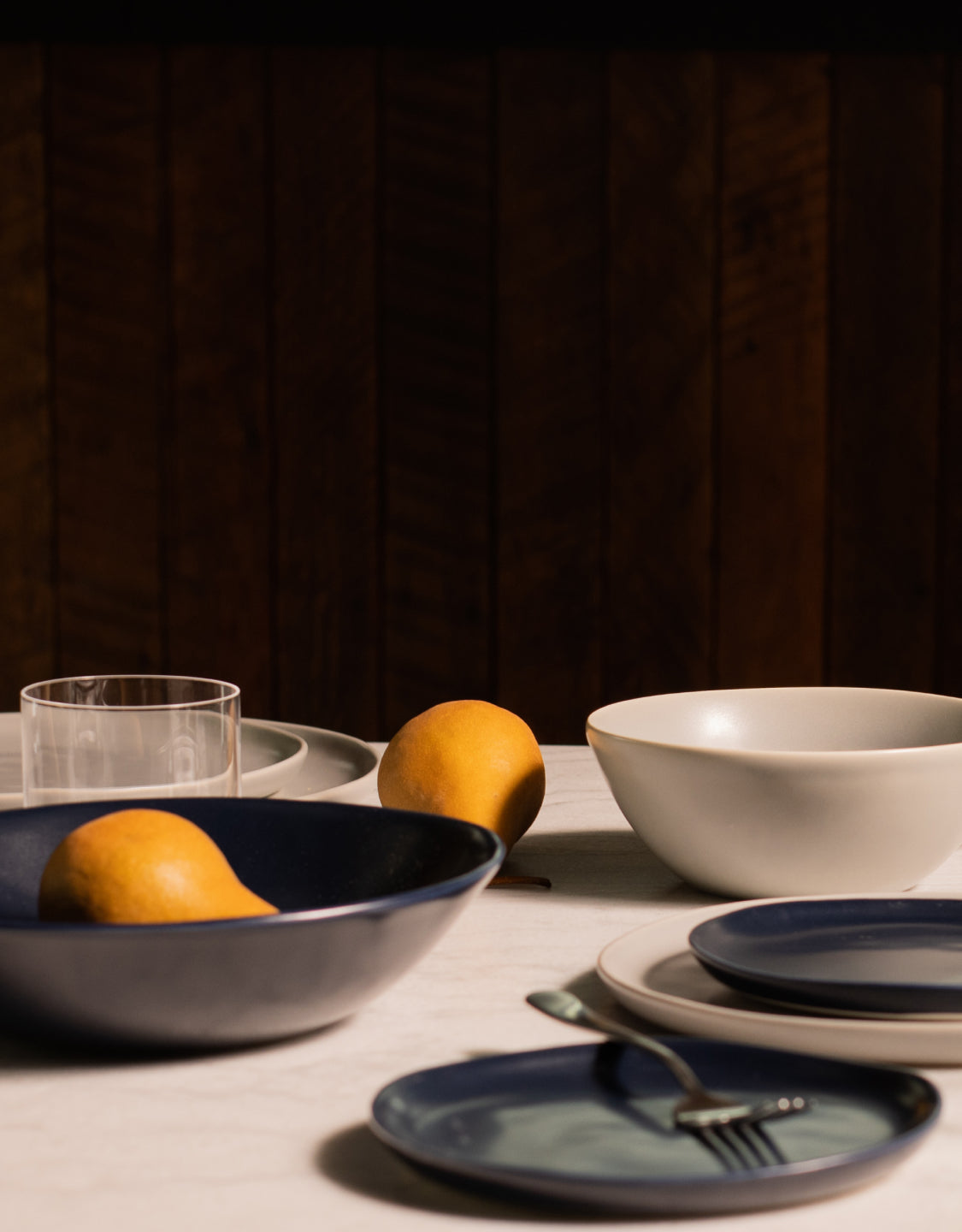 Fable white and navy dinnerware with clear glasses and lemons on a marble table against a dark wood wall