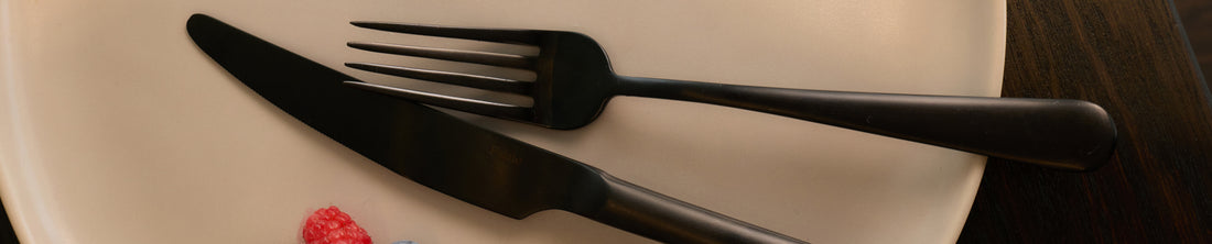 Black fork and knife resting on a cream ceramic plate with raspberries