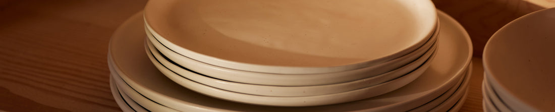 Stacked warm-toned ceramic dinner and dessert plates on a wood surface in golden light