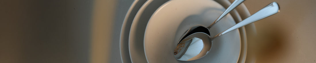 Two silver spoons resting inside nested white ceramic bowls, top-down close-up view