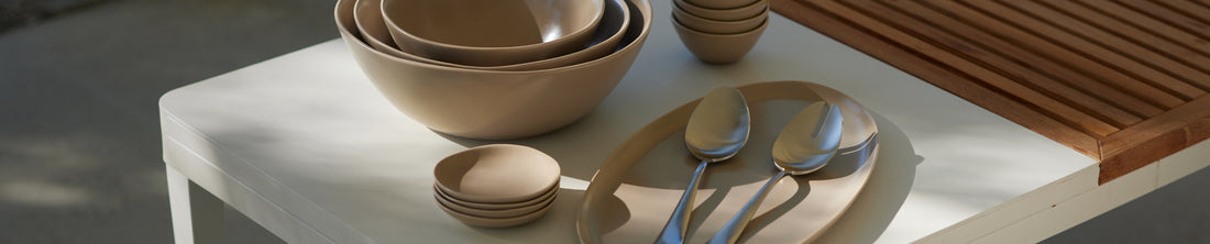 Fable taupe nested bowls and serving plate with silver spoons on a white outdoor table