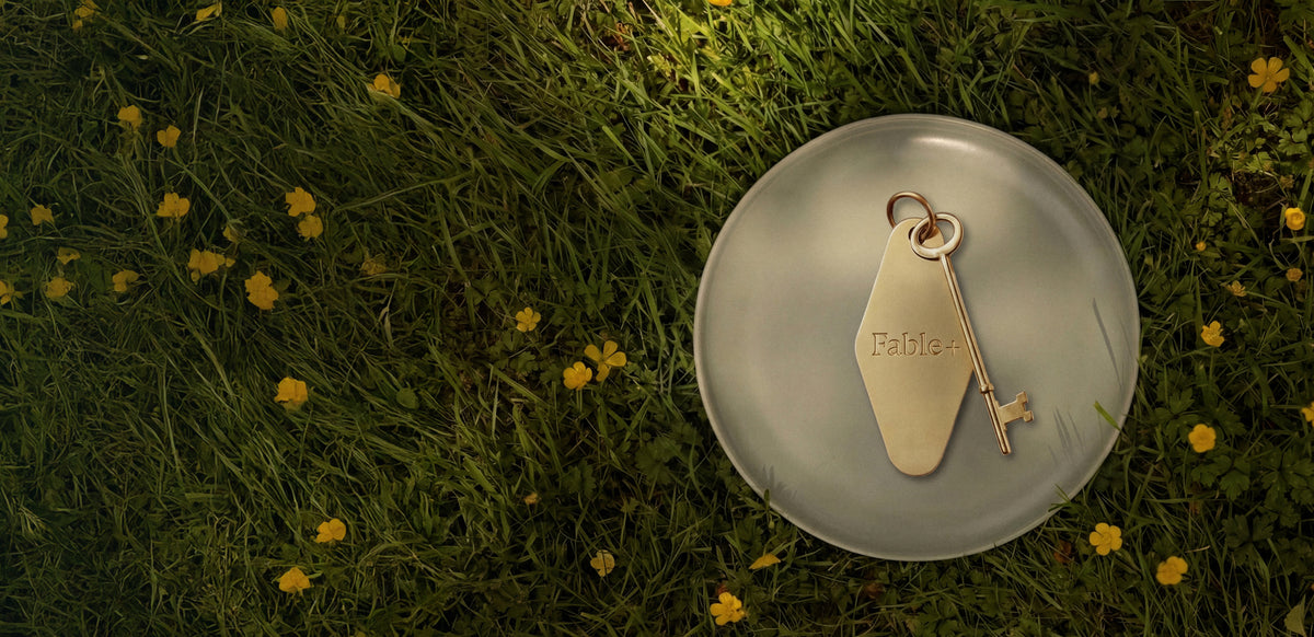 Brass Fable+ membership keytag resting on a stoneware plate among grass and yellow buttercups