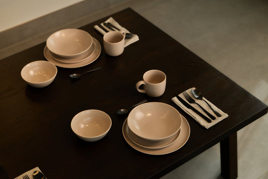 Fable beige matte stoneware place settings with black flatware on a dark wood dining table