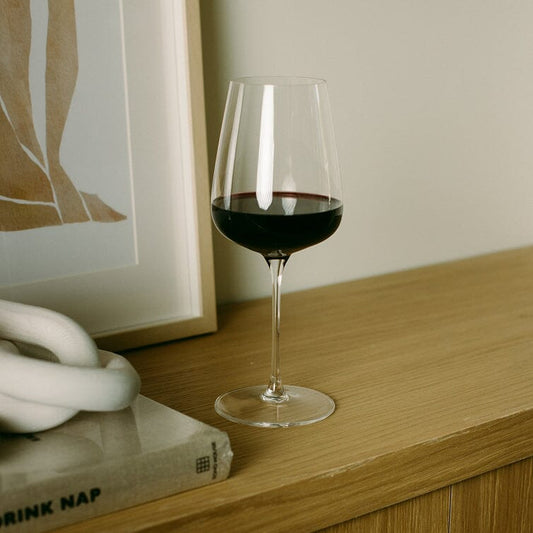 Wine glass with red wine on a wooden surface next to a framed picture and a book. #clear