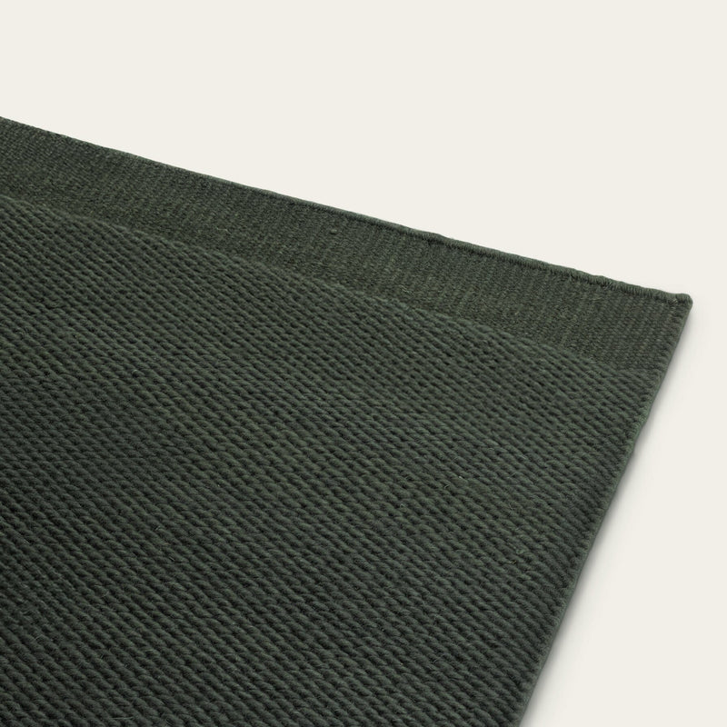Close-up of a dark green woven rug corner on a light gray background #forestgreen